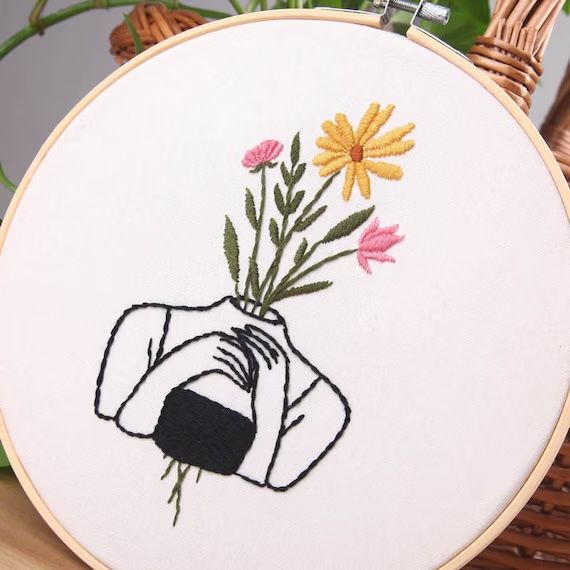 bastidor cojn ilustracion bordada de chica dibujada a linea negra y con ramo de flores que hace no se vea la cara